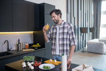 Smiling man with glass of juice standing near the table.