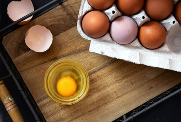 Bowl of raw egg and egg shell on a wooden tray.