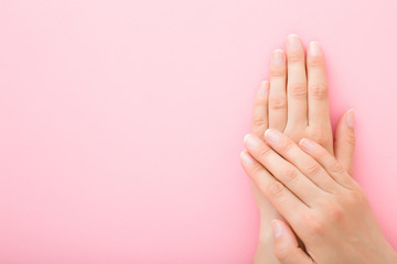 Young woman hands without nail polish on light pink background. Pastel color. Simple manicure. Closeup. Empty place for text. Top down view. - obrazy, fototapety, plakaty