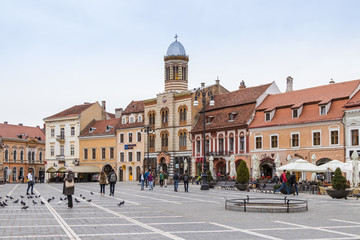 Fototapeta na wymiar Tourists walk in the Square of Council Market around the Historical Museum and see the sights in the Old Town of Brasov in Romania