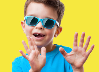 Little boy in sunglasses raised his hands up, on yellow background