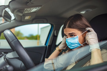Woman during pandemic isolation at city, she is in car. Young woman driving car with protective mask on her face. Healthcare, virus protection, allergy protection concept.