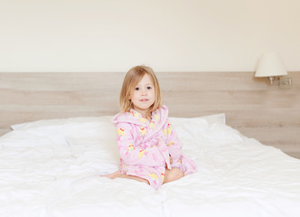 Naklejka premium Happy morning! little girl sitting in a bathrobe on the bed