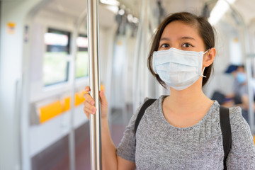 Fototapeta na wymiar Young Asian woman wearing mask and standing with distance inside the train for protection from corona virus outbreak