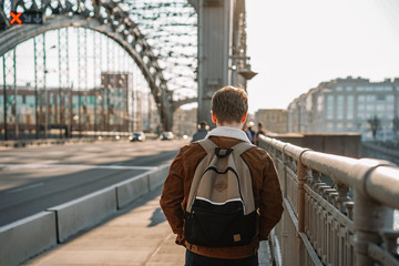 Photo from the back as a young business programmer walks on a metal bridge in a Sunny beautiful sunset