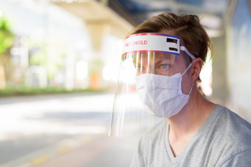 Young man with mask and face shield at the bus stop for protection from corona virus outbreak