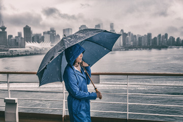 Rain storm Asian woman outside with umbrella watching Vancouver city on cruise ship background.