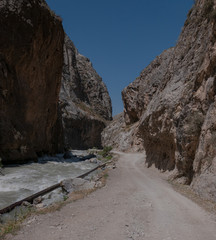mountains of Central Asia. a narrow road between mountains. rapid river and sparse vegetation. there are no people.