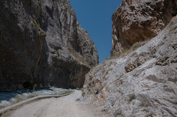 mountains of Central Asia. a narrow road between mountains. rapid river and sparse vegetation. there are no people.