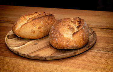 Freshly made sourdough bread on a wooden plater. The two loafs are golden and crusty