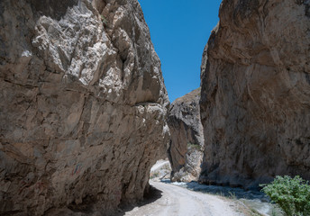 mountains of Central Asia. a narrow road between mountains. rapid river and sparse vegetation. there are no people.