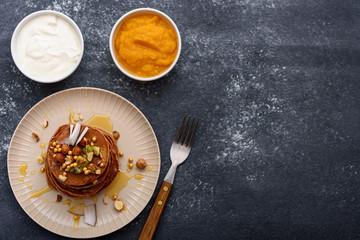 vegetarian chocolate pancakes with nuts, maple syrup, fruit, mango jam, sour cream on gray background, copy space, top view