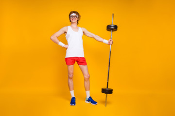 Full length body size view of his he nice attractive cheerful cheery content slim thin fit sportive guy holding in hand heavy barbell isolated over bright vivid shine vibrant yellow color background