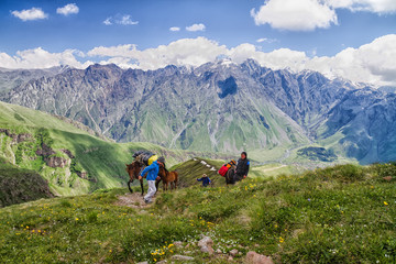 KAZBEGI, GEORGIA - JUNE 23L Men with horses carrying backpacks at Caucasus mountains on June 23,...