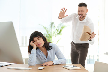 Fototapeta premium Man popping paper bag behind his sleeping colleague in office. April fool's day