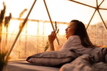 Happy woman is relaxing on bed in a tent around mountains under sunset light sky enjoying the pleasure and freedom Traveling along the mountains, freedom and active lifestyle concept.