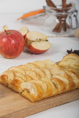 Close-up of Small apple pie with brioche dough on wooden cutting board with various ingredients. vertical image