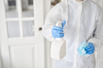 Closeup of a white spray bottle in woman hands in a protective suit and blue gloves. Disinfection, cleaning and washing. COVID-19. Prevention of coronavirus infection.