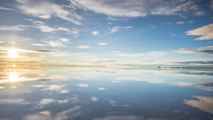 Naklejka na ściany i meble Misty landscape with clouds and sun reflection in the lake , early morning, calm and quiet, pastel blue and golden color, Salar de Uyuni, Bolivia