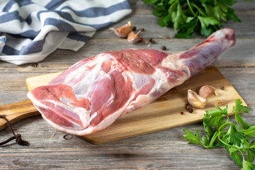 Raw mutton leg on a bone on a wooden Board on a gray wooden table. Sheep meat close-up. A fresh...