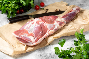Raw mutton leg on the bone on parchment on the gray kitchen table. Sheep meat close-up. A fresh...