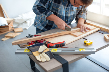 Asian craftsman carefully sanding wood plank in workshop studio,