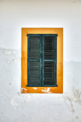 Green old wood shutters with yellow painted frame on a white deteriorated wall