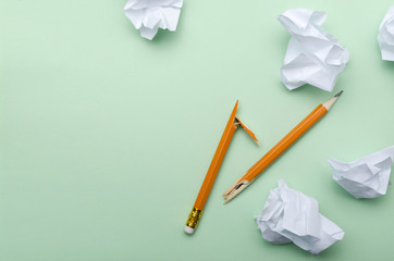 Top view of broken pencil, crumpled white piece of paper on the green surface.Empty space.Concept...
