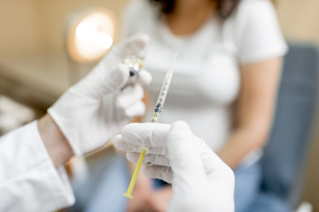 Doctor holding vaccine or some medication in the syringe, preparing for injection for a pregnant...