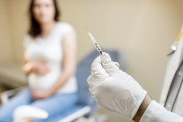 Doctor holding vaccine or some medication in the syringe, preparing for injection for a pregnant...