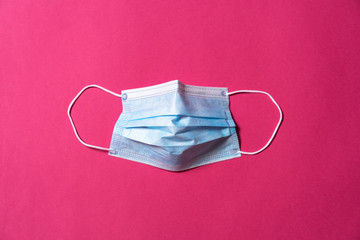 Surgical mask with the shape of the face for personal protection from virus and epidemics shot from above on a dark pink background - Concept photo of the Coronavirus, Covid-19