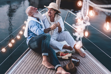 Senior couple cheering with champagne on a sailboat during summer vacation - Old people having fun...