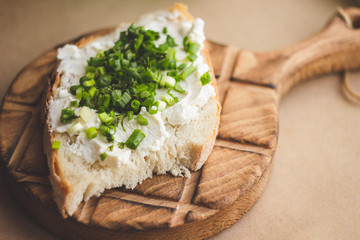 Bread with curd cheese and green onions on a wooden stand; close-up of a sandwich for a spring breakfast