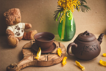 Arrangement of yellow flowers in a green vase, a teddy bear and a Chinese cup of tea; warm tinting