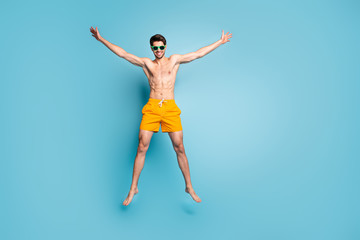 Fototapeta na wymiar Full length body size view of his he nice attractive cheerful cheery funky guy in swimming shorts jumping up having fun isolated on bright vivid shine vibrant green blue turquoise color background