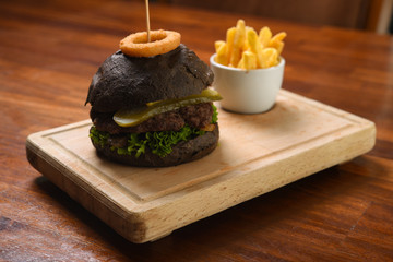 Homemade black hamburger with beef, cheddar, tomato, lettuce and sweet and sour sauce. French fries, onion rings. Serve on a wooden kitchen board. background image, copy space