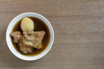 top view of boiled pork rib and duck egg with sweet brown soup in a ceramic bowl on wooden table. asian homemade style food concept..
