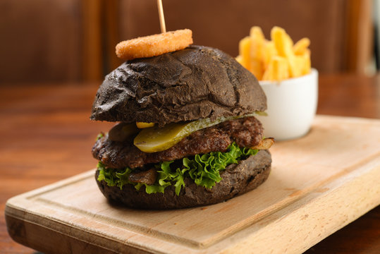 Homemade black hamburger with beef, cheddar, tomato, lettuce and sweet and sour sauce. French fries, onion rings. Serve on a wooden kitchen board. background image, copy space