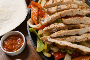 Detail of chicken fajitas served with sauces on wooden floor