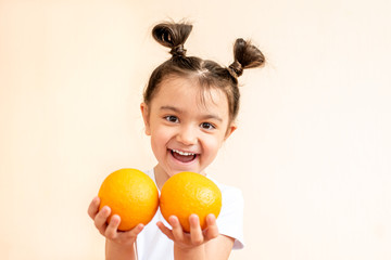 Fototapeta na wymiar A little girl in a white T-shirt holds two orange oranges in her hands. A girl in a white T-shirt laughs and holds two oranges in her hands. 