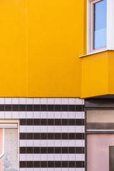 A facade of a house with a yellow concrete wall and black and white tiles. Different colors and textures in the exterior of a building. Vertical shot