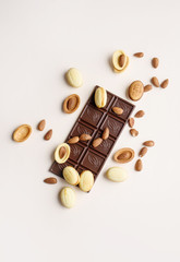 A bar of chocolate lies on a light background with almonds, walnuts, nuts with boiled condensed milk.