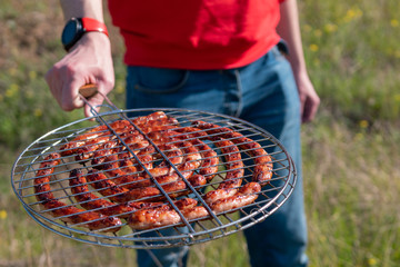 Man holding grilling basket with roasted sausages. Grilling sausages on barbecue grill. BBQ outside. Bavarian sausages.