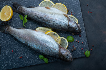 Rainbow trout with lemon on a dark cutting board. Red pepper and basil. Two fishes