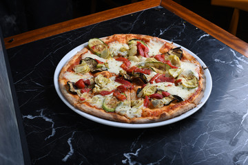 pizza with arugula decoration consisting of eggplant, zucchini, cheddar cheese slices, red pepper on black marble table