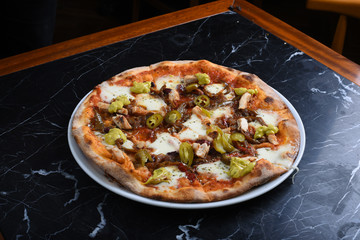 pizza with jalapeno peppers, chicken, cheddar and pizza sauce on black marble floor