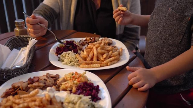 Lunch on a white plate. Fast food, gyros, french fries, beetroot and cabbage salads. The woman eats meat and salad. The child puts the fries away and, together with the mother, they leave the table.