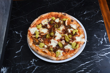 pizza with jalapeno peppers, chicken, cheddar and pizza sauce on black marble floor