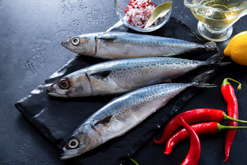 3 fresh raw fish mackerel, chili pepper, lemon, oil, spices on a black background