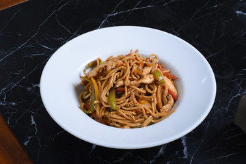 chinese cuisine, noodles on a black background, served with meat, chicken, vegetables, red pepper